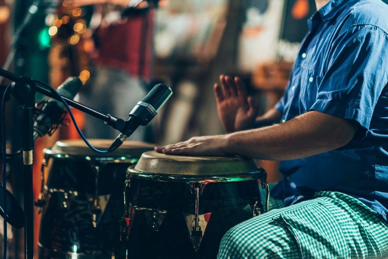 A person playing drums with microphones in the background.